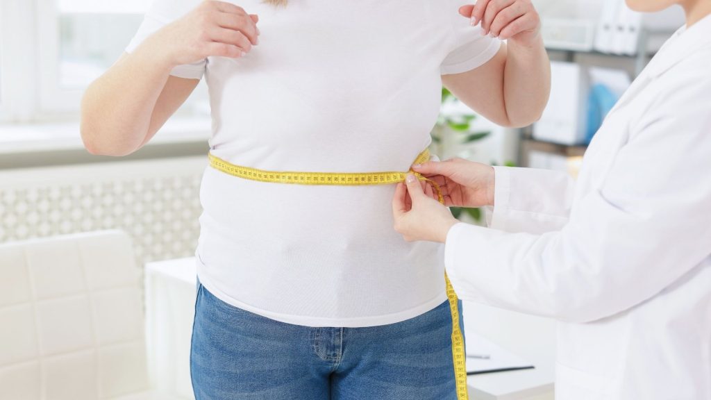 a doctor uses a measuring tape on a weight loss patient